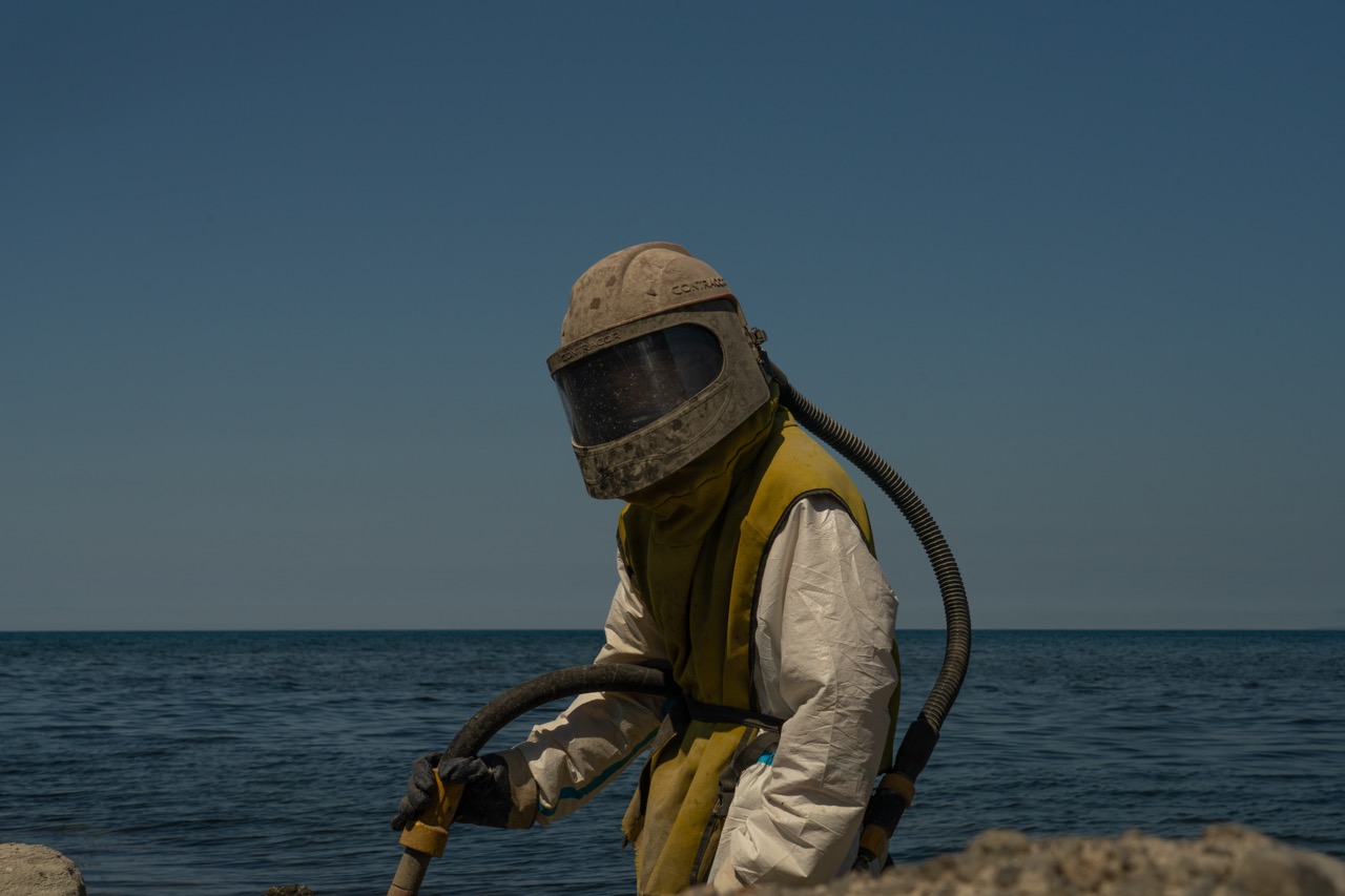 Groß (1 - An Emergencies Ministry employee in a dust-proof suit cleans rocks from fuel oil.jpeg